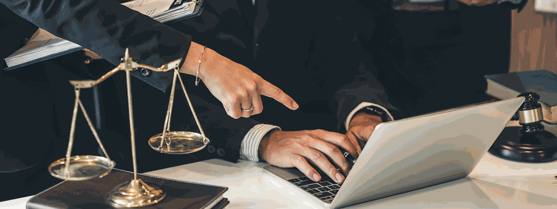 Two people discussing at a laptop with legal scales in the foreground.