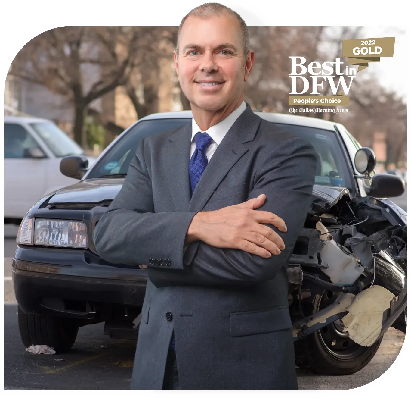 A smiling man in a suit stands in front of a damaged car, with a "Best in DFW" award banner.