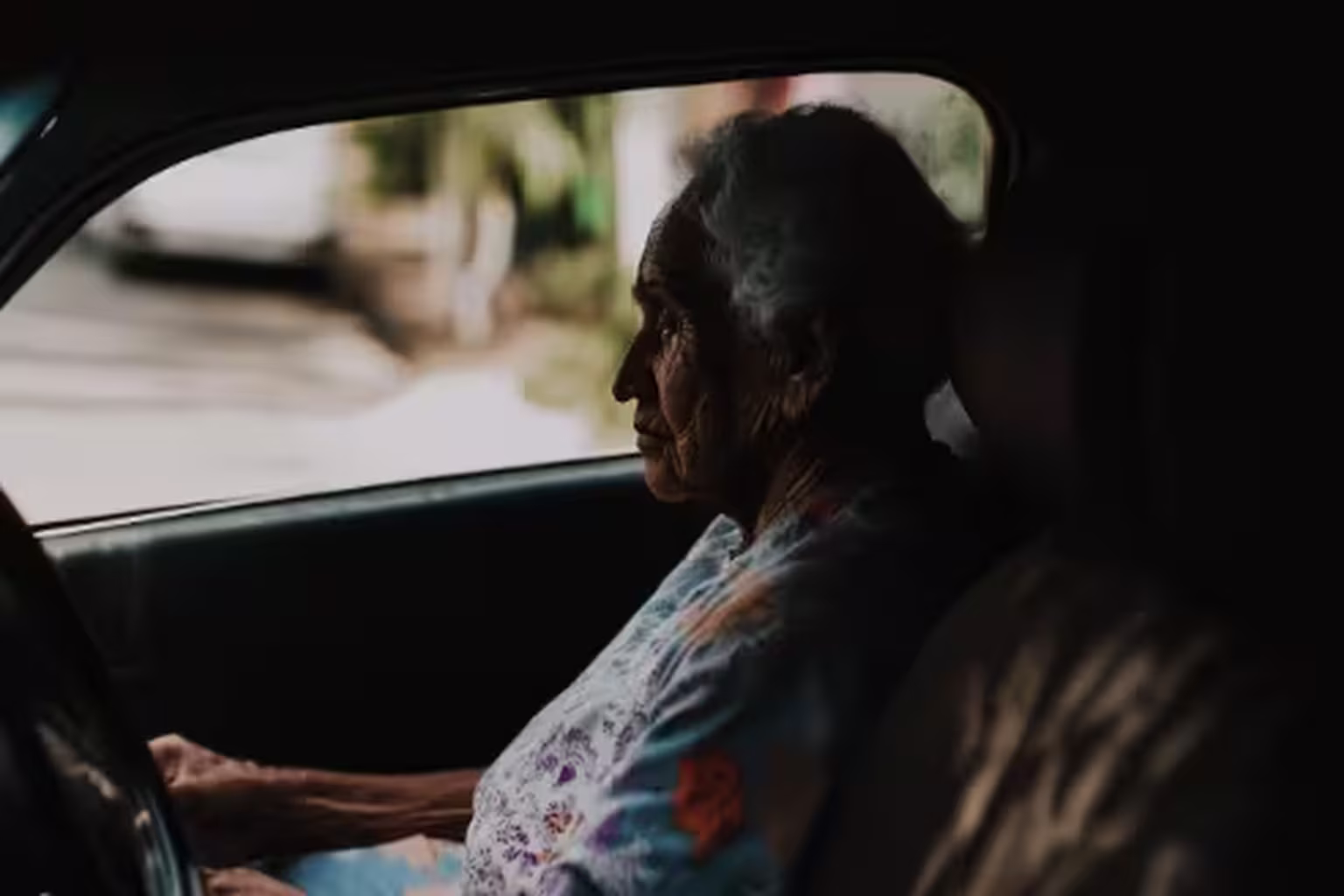 Elderly woman sitting in a car, looking out the window.