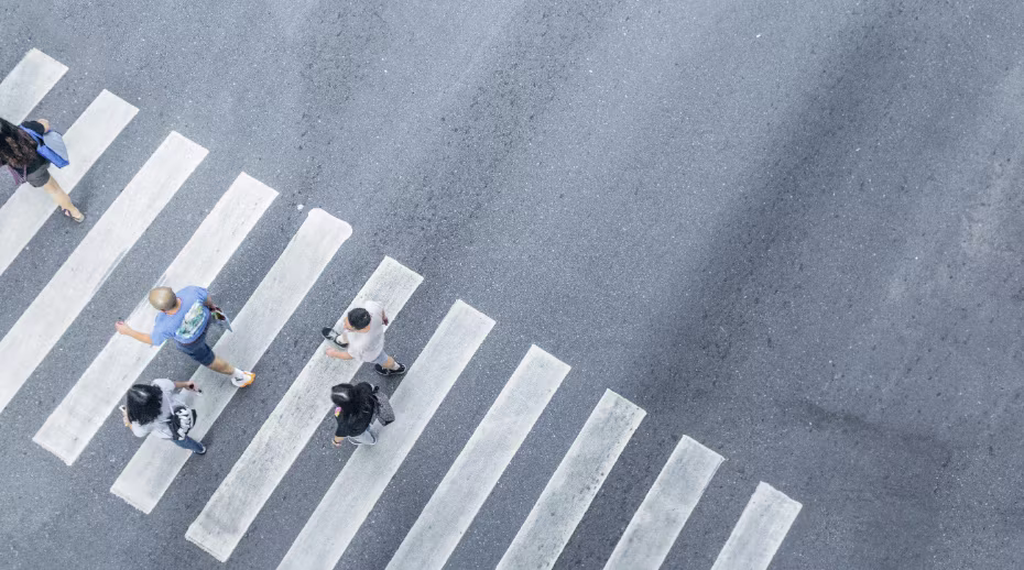 Aerial view of pedestrians walking across a crosswalk on an urban street.
