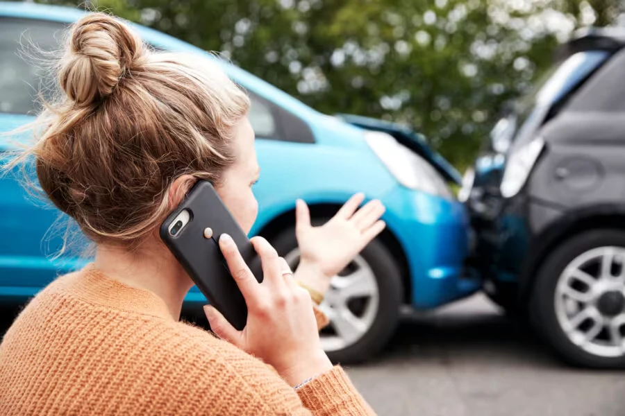 Woman on phone after rear-end car accident between a blue car and a black car.