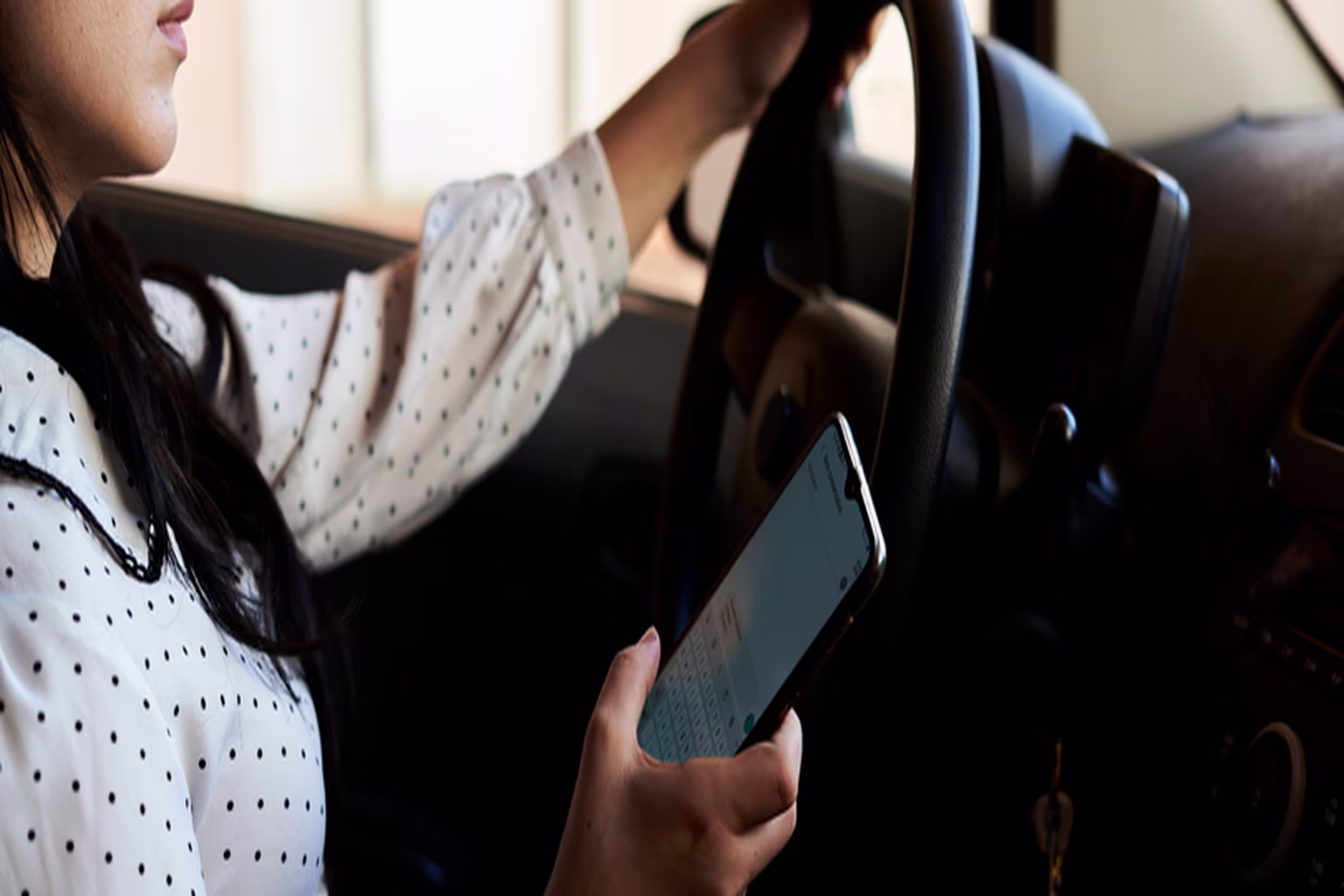 Driver holding smartphone while behind the wheel of a car, demonstrating distracted driving behavior