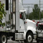 White commercial semi-truck at a gas station with fuel pumps visible in the background
