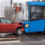 Red SUV collided with blue city bus at urban intersection with traffic lights visible in background