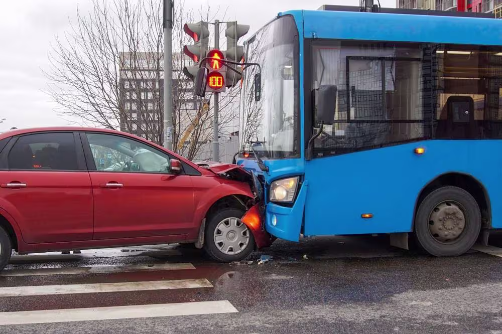 Red SUV collided with blue city bus at urban intersection with traffic lights visible in background