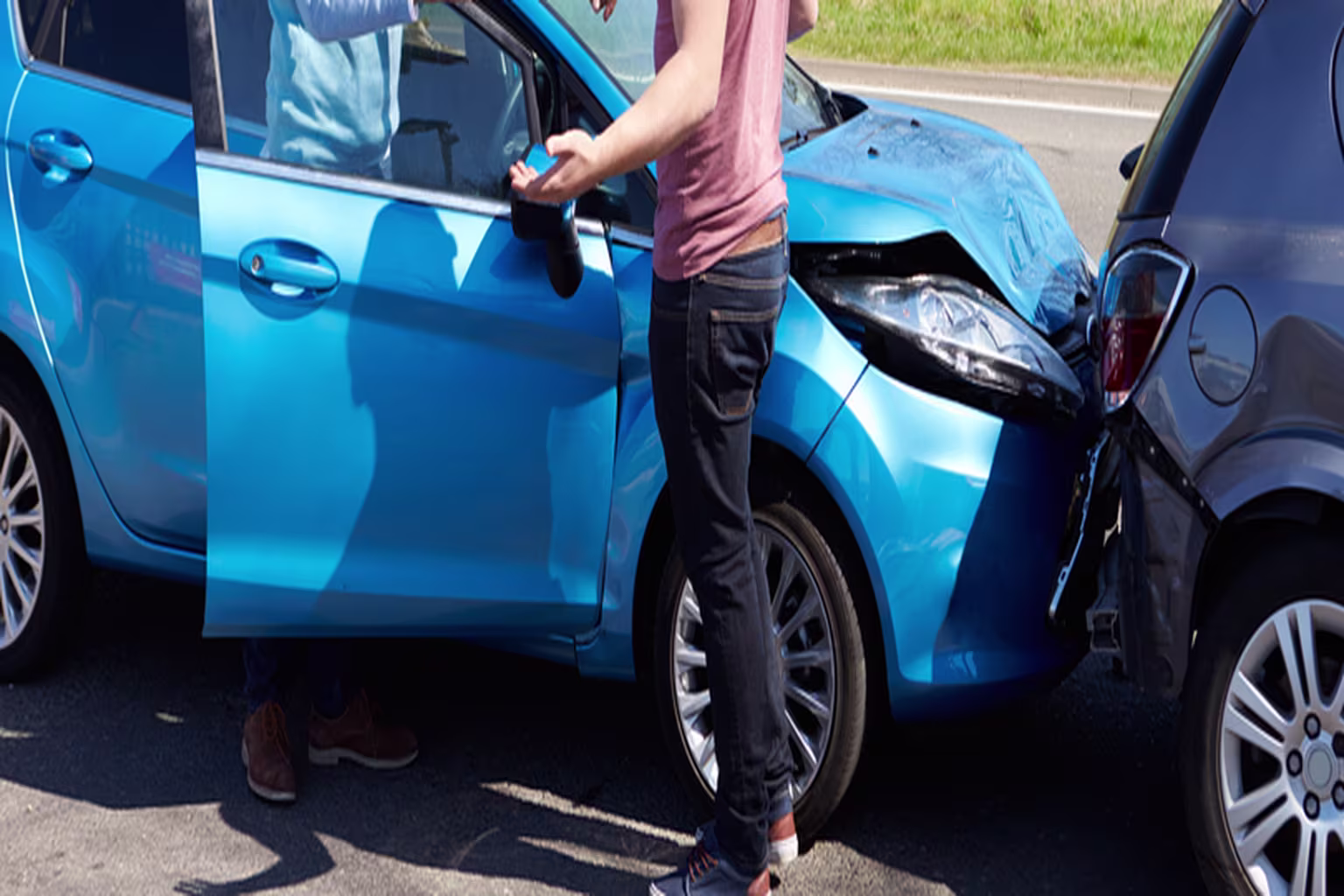Two drivers inspect damage after a rear-end collision between a blue car and a gray car.