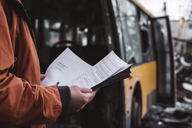 Person holding legal documents in front of damaged public transit bus, illustrating the importance of proper documentation and legal representation for public transportation accident claims
