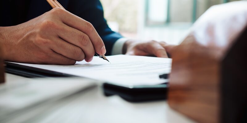 A person signing a document with a pen on a table