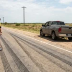 Two police officers and a couple look at roadside skid marks after a crash.