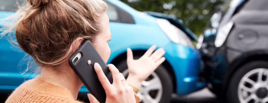 Woman on phone after rear-end car accident between a blue car and a black car.