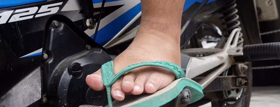 Person's foot wearing turquoise flip-flop on motorcycle footrest, demonstrating risky footwear choice for riding