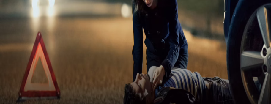 A person assists an injured individual on a road at night.