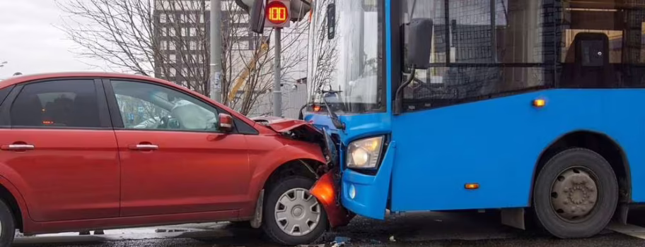 Red SUV collided with blue city bus at urban intersection with traffic lights visible in background