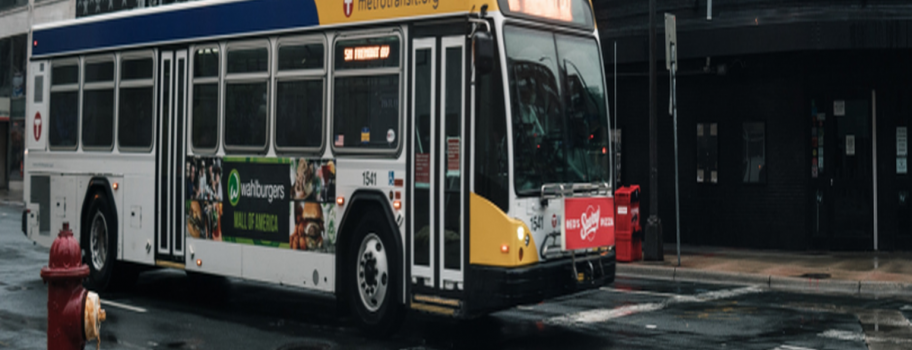 Metro Transit bus on wet city street with urban buildings in background