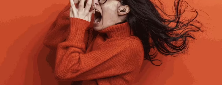 Frustrated woman in an orange sweater yelling into her phone against an orange background.